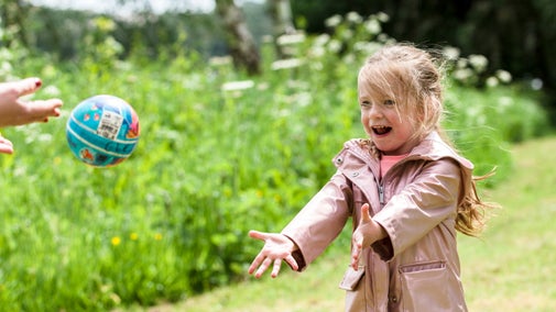 Image shows a child giggling as she reaches out to catch a ball.